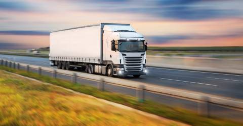 Een witte vrachtwagen onderweg op de grote weg bij ondergaande zon